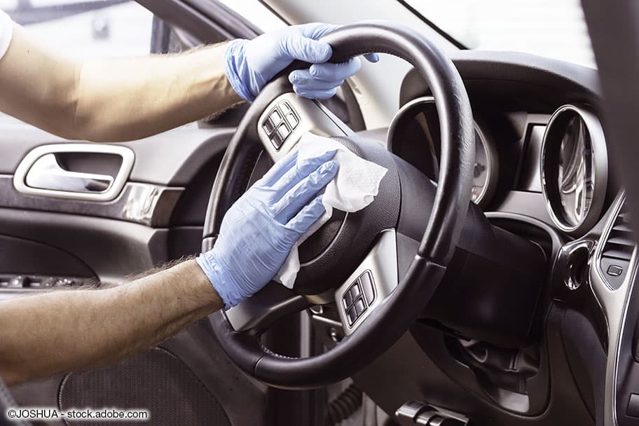 Ein Mann desinfiziert das Lenkrad seines Auto mit einem Desinfektionstuch und blauen Putzhandschuhen.
