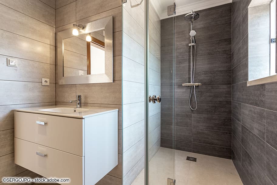 Waschtisch mit Spiegel und daneben ebenerdige Dusche mit Wandfliesen und Glastüre