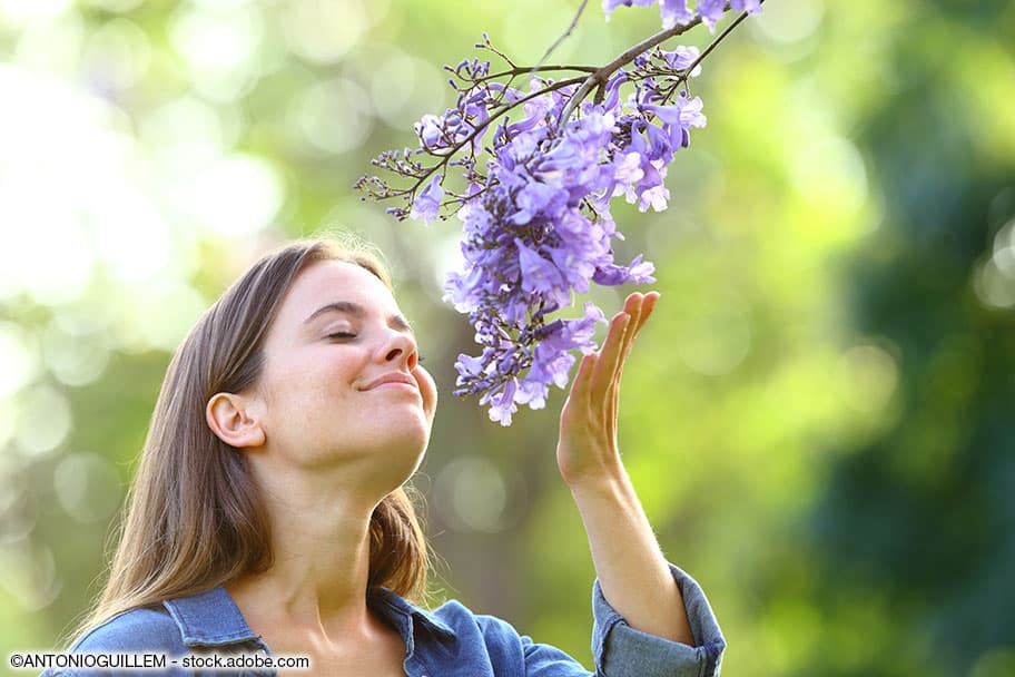Junge Frau riecht in der freien Natur an violetten Blumen.