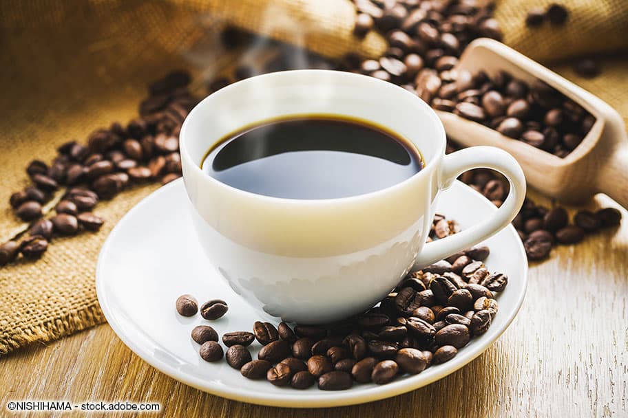 Eine Tasse voll frisch gemahlenem Kaffe, umgeben von Kaffeebohnen.