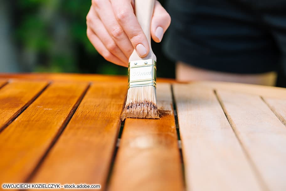 Holzpflege wird mit einem Pinsel auf einen Holztisch aufgetragen.