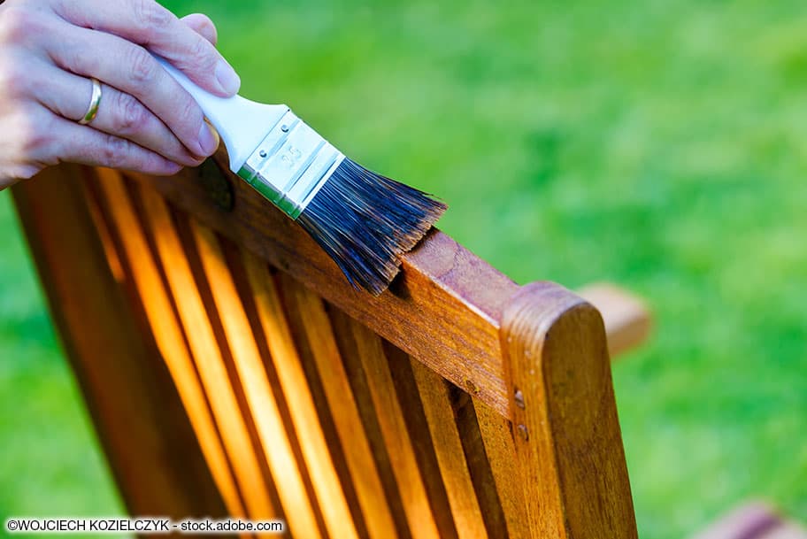 Gartenstuhl aus Holz wird mit einem Pinsel geölt.