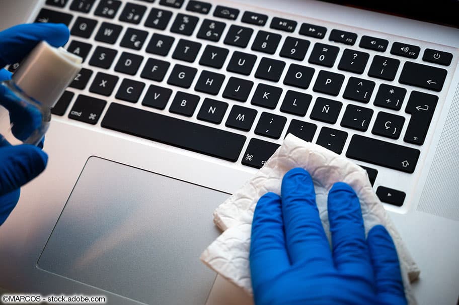 Abreiben mit blauen Gummihandschuhen von PC-Tastatur mit weissem Lappen und Desinfektionsmittel.