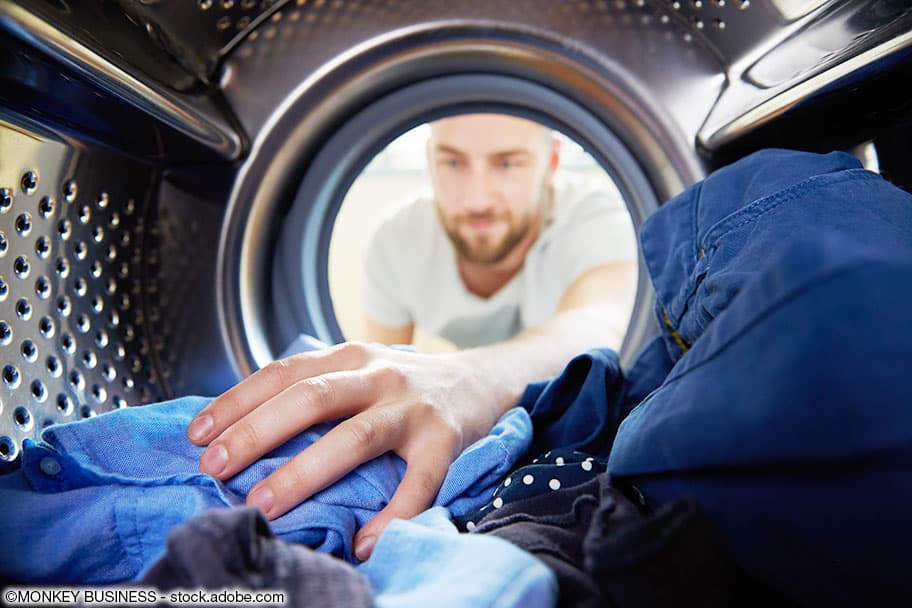 Ein Mann legt seine blaue Wäsche in eine Waschmaschmaschine.