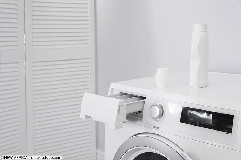 Weisse Waschmaschine mit offenem Fach in einem weissen Raum.